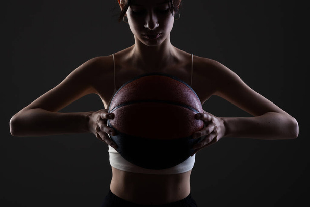 Teenage girl with basketball. Side lit studio portrait against dark background. - Zdjęcie, obraz
