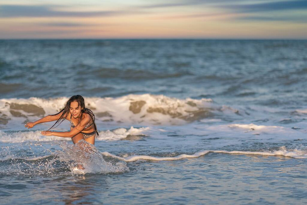 A girl with loose hair walks on the sea with waves and enjoys the sun - Photo, image