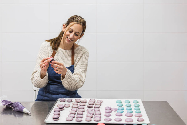 Cheerful woman making macaroons in bakery in bakehouse - Photo, Image