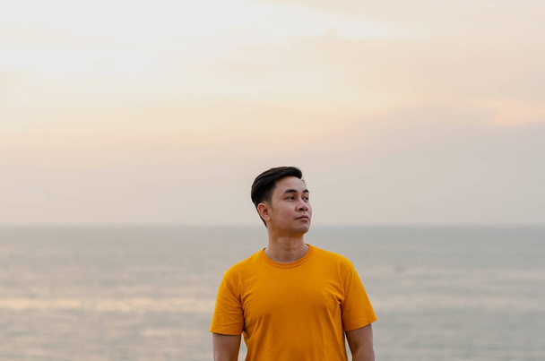 Ázsiai férfi mosolyog és felnéz a tenger és az ég hátterével. Jó mentális egészség koncepció. - Fotó, kép