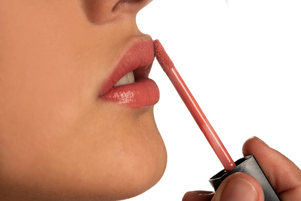 Nahaufnahme einer Frau, die einen Lipgloss auf ihre Lippen auf weißem Hintergrund aufträgt - Foto, Bild