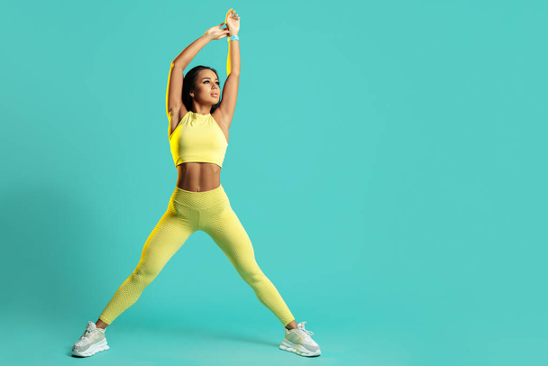 Full lengh image young brunette woman stretching before exercise set over blue background. - Φωτογραφία, εικόνα