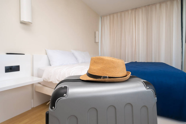 Otel odasında üzerinde hasır şapka olan gri bir valizin yakın çekimi. Seyahat, tatil kavramı - Fotoğraf, Görsel