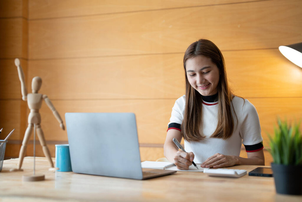 Smiling girl student wear taking note for study online with teacher, happy young woman learn language listen lecture watch webinar write notes look at laptop at home, distant education. - Φωτογραφία, εικόνα