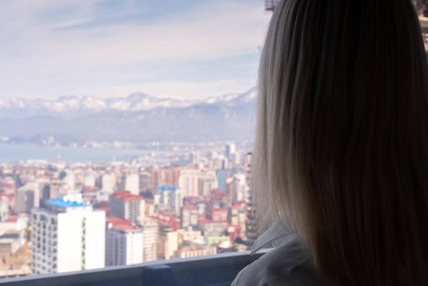 Retrato de una mujer rubia desde atrás mirando desde una altura a una ciudad borrosa y montañas en un día soleado, espacio para copiar - Foto, imagen