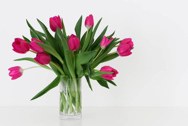 Tulip flowers in a transparent small vase standing on white table. Bouquet of spring flowers - Fotoğraf, Görsel