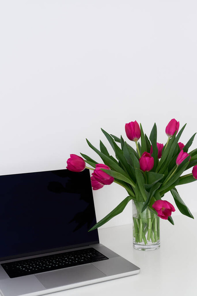 Laptop ve bir vazo dolusu taze lale çiçeği beyaz bir masada vazoda. Serbest yazar, girişimci veya blogcu çalışma alanı - Fotoğraf, Görsel