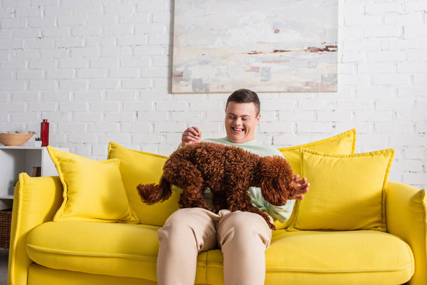 Adolescente positivo com síndrome de down brincando com poodle marrom na sala de estar  - Foto, Imagem