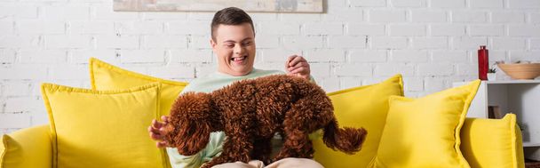 Boldog fiú Down-szindróma játszik uszkár a kanapén, banner  - Fotó, kép