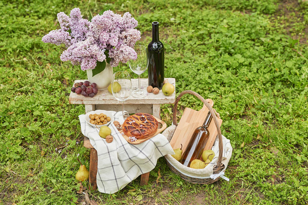 Summer picnic in garden. Wine, pie, fruits and flowers. Still life. Easter lunch and table. - Foto, imagen