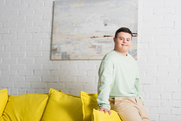 Teenager with down syndrome looking at camera near couch at home  - Fotó, kép