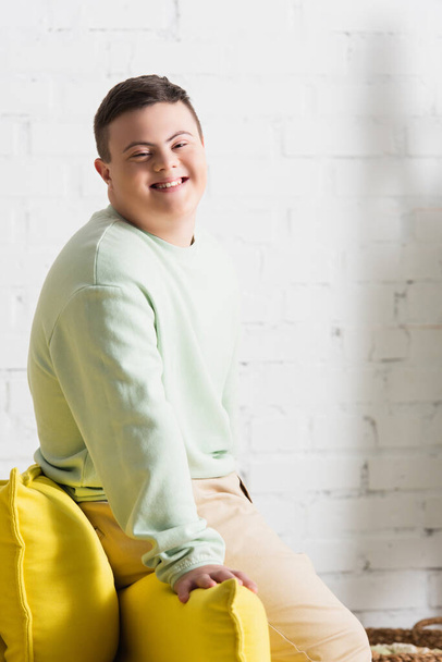 Positive teenager with down syndrome looking at camera near couch in living room  - Foto, afbeelding