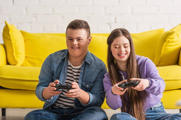 KYIV, UKRAINE - JANUARY 21, 2022: Positive teenagers with down syndrome playing video game at home  - Fotografie, Obrázek