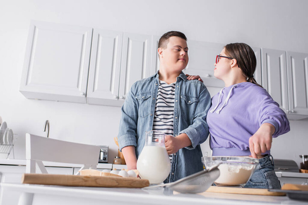 Low angle view of teenager with down syndrome cooking near boyfriend at home  - Foto, immagini