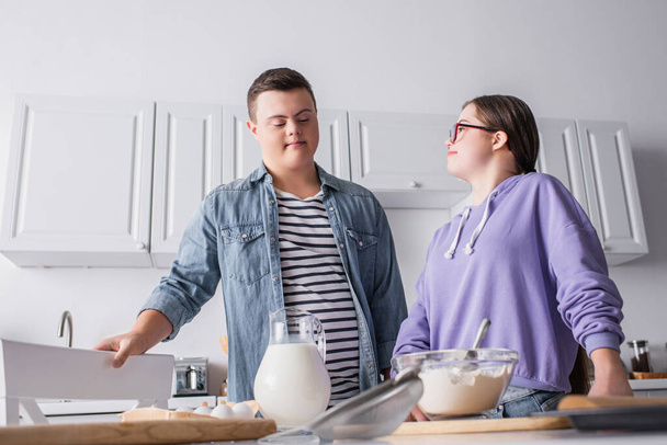 Nízký úhel pohledu na pár s Downovým syndromem stojící v blízkosti složek v kuchyni   - Fotografie, Obrázek