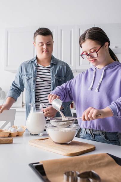 Teenager με σύνδρομο down μαγείρεμα κοντά στο φαγητό και ο φίλος στην κουζίνα  - Φωτογραφία, εικόνα