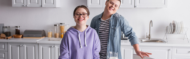 Adolescentes positivos con síndrome de Down mirando a la cámara en la cocina, pancarta  - Foto, imagen