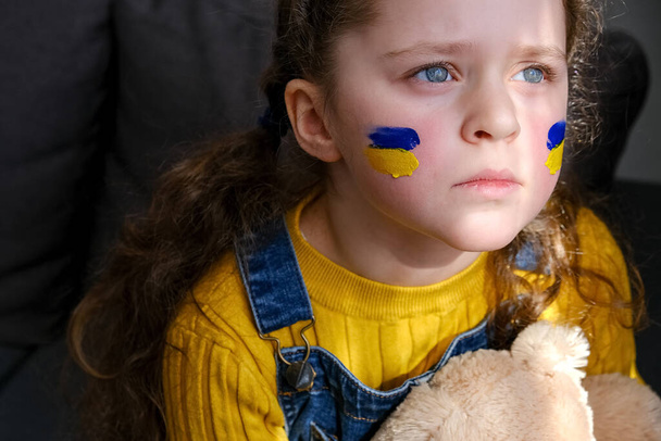 Portrait of upset sad little girl child with flags of ukraine on face. Peace, no war, help, stop russian aggression. Freedom to Ukraine, Crisis concept. Hope for the world. Anxiety and anticipation - Zdjęcie, obraz