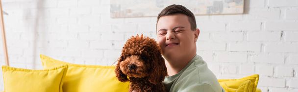 Positive boy with down syndrome closing eyes near poodle at home, banner  - Photo, Image