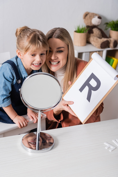 Girl and speech therapist with clipboard talking near mirror in consulting room  - Photo, Image
