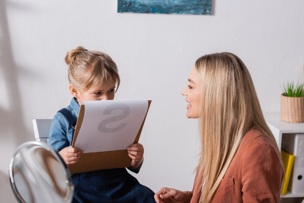 Speech therapist talking near child holding clipboard in classroom  - Φωτογραφία, εικόνα