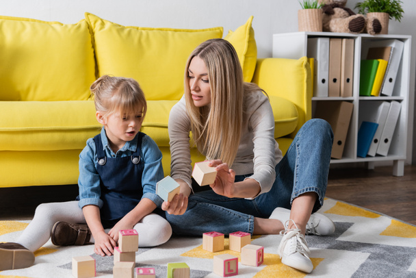 Speech therapist holding wooden blocks near child in consulting room  - Фото, изображение
