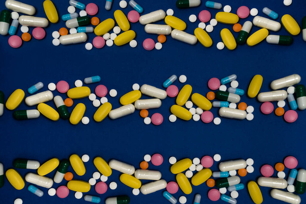 Fondo azul con espacio de copia y muchos medicamentos en cápsulas y tabletas de diferentes colores dispersos en la superficie - Foto, Imagen