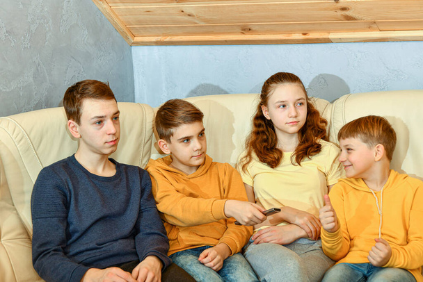 Four children with a TV remote sit on a yellow leather sofa next to a glass coffee table. - Fotoğraf, Görsel