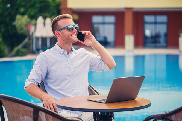 Молодий чоловік бізнесмен з ноутбуком сидить біля басейну. Відкрите робоче місце. Концепція фрілансера. Інтернет-магазини. Відпустка роботи
 - Фото, зображення