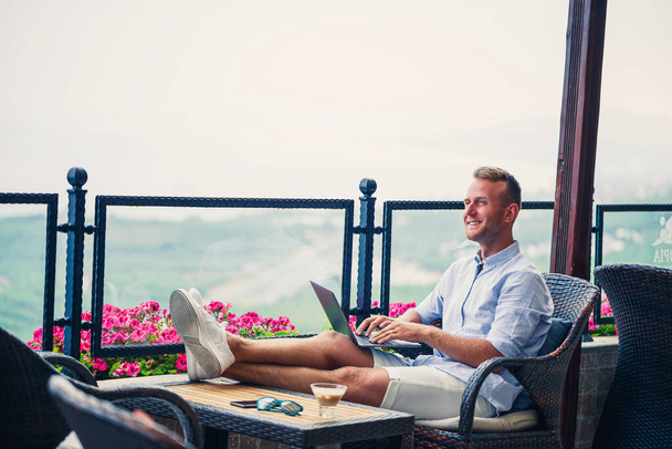 Sikeres férfi üzletember dolgozik nyaralás mögött egy laptop hegyi kilátással. Online menedzser munkafolyamat. Munka a szabadban, gyönyörű kilátással az erkélyről - Fotó, kép
