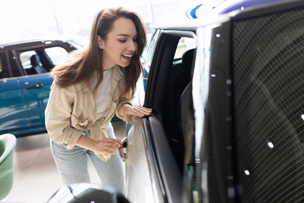 młoda kobieta bada go w salonie samochodowym przed zakupem samochodu - Zdjęcie, obraz