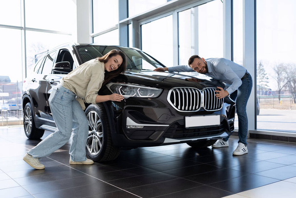 junges Ehepaar umarmt freudig das Auto und freut sich über den Kauf eines neuen Autos - Foto, Bild