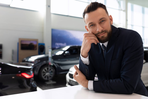 portret van een medewerker van een autodealer in de showroom tegen de achtergrond van nieuwe auto 's - Foto, afbeelding