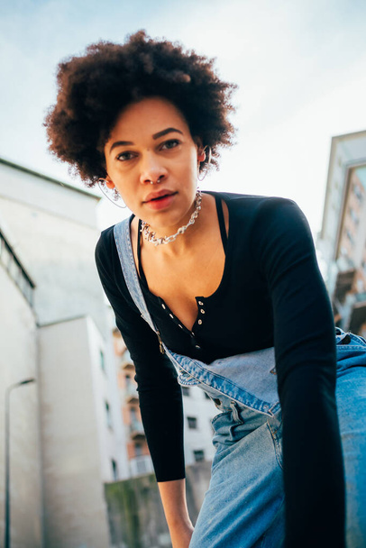 Nuori mixed race kihara tukka nainen poseeraa ulkona muodikas näköinen kamera luottavainen - Valokuva, kuva