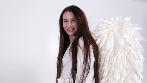 Bruneta dívka v bílých šatech s andělskými křídly na bílém pozadí ve studiu - Záběry, video