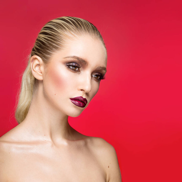 Retrato de primer plano de una joven modelo femenina, mirando a un lado, con un maquillaje perfecto con hombros desnudos, aislado sobre un fondo rojo. - Foto, Imagen