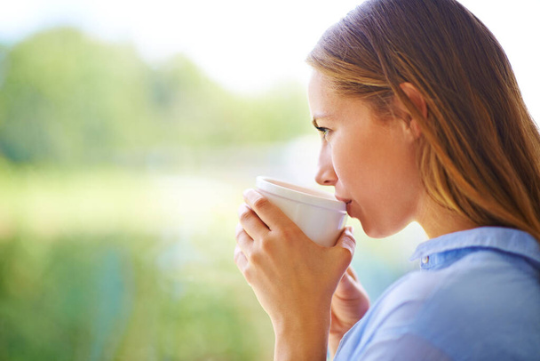 Contentment in a cup. Cropped shot of a young woman having coffee while standing by a window. - Foto, Imagem