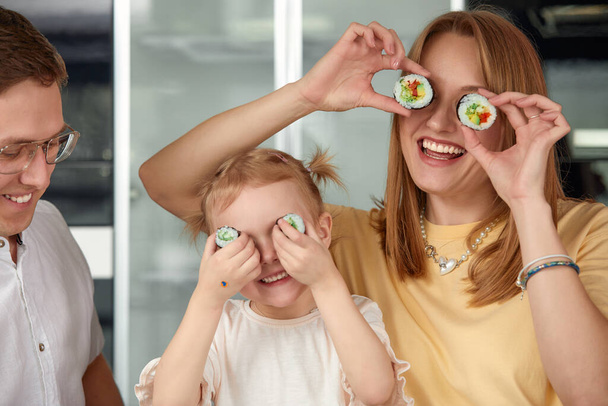 Happy caucasian family having fun and eating sushi and rolls in the kitchen at home. Delivery food concept - Foto, Imagem