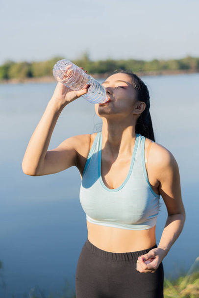 Asyalı kadınlar koşudan sonra su içer, temiz plastik şişelerle spor yapar ve parkta size gülümser.. - Fotoğraf, Görsel