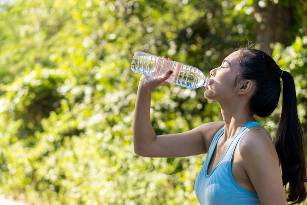 アジアの女性はジョギング後に水を飲み、透明なペットボトルでスポーツをしたり、公園であなたを笑顔にしたり. - 写真・画像