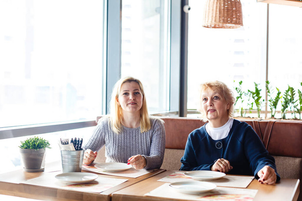 Két boldog nő beszélget a kávézóban. Egy idős nő és a felnőtt lánya kávéznak a kávézóban. Anyák napja. - Fotó, kép
