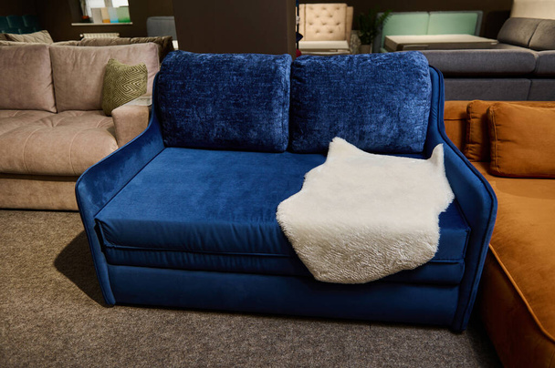 Exposición de sofás y sofás con diferente calidad y textura de tejidos en la sala de exposiciones de una tienda de muebles. Concéntrate en un pequeño sofá cómodo azul, que se muestra en venta - Foto, imagen