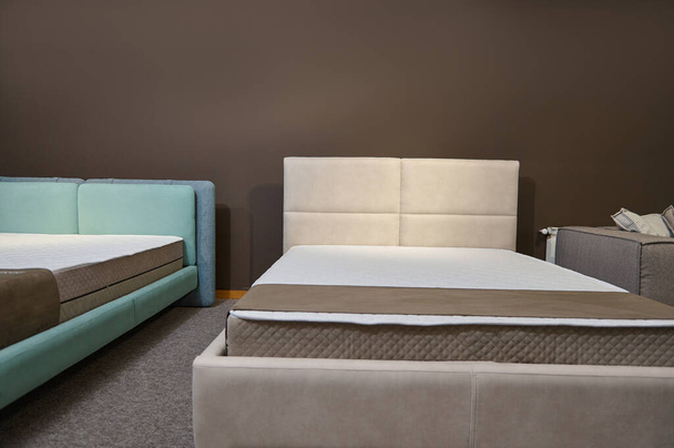 Современные стильные розовые и синие велюровые двуспальные кровати с ортопедическими жесткими матрасами, выставленные в демонстрационном зале мебельного магазина - Фото, изображение
