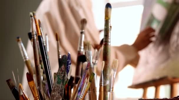 Estudio de arte - mujer artista en camisa blanca cambiando pinceles y dibujando una pintura - Metraje, vídeo