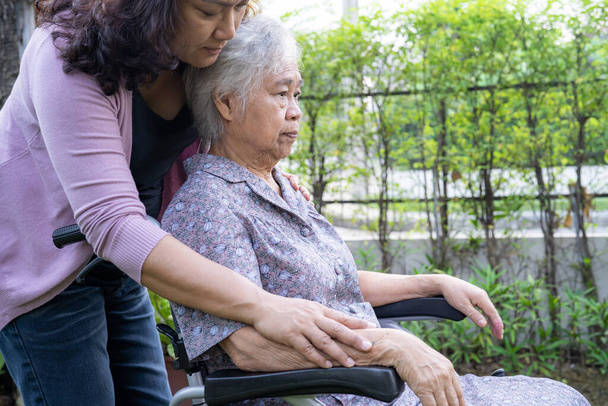 Hija cuidadora ayuda asiática anciana o anciana anciana en silla de ruedas eléctrica en parque. - Foto, imagen