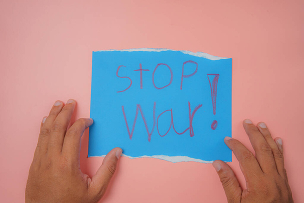 Die Hand des Mannes hält ein blaues Papier mit der Aufschrift Stop War auf rosa Hintergrund Kein Krieg, Stop War, Russische Aggression. - Foto, Bild