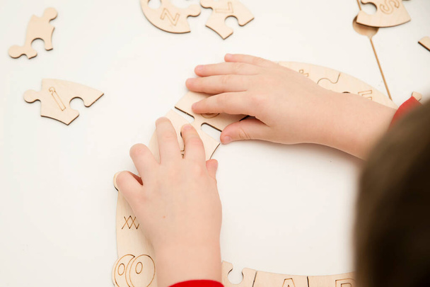 3D wooden toy. Learning letters in order of alphabet. Child's fingers holds pieces of unfinished to assemble puzzle. - Foto, Imagen