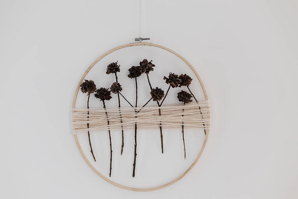 ドライな花でスタイリッシュなboho秋の花輪。木製のフープ、糸、乾燥したハーブの花輪は白い壁にかかっています。現代の花の配置と創造的な手作りの装飾 - 写真・画像