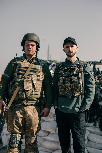 Ουκρανός πολεμιστής εδαφικής άμυνας στέκεται κοντά εθελοντής στο σημείο ελέγχου στο σώμα πανοπλία με αυτόματο όπλο. Έννοια της ρωσικής στρατιωτικής εισβολής στην Ουκρανία. Πόλεμος στην Ουκρανία και την Ευρώπη. - Φωτογραφία, εικόνα