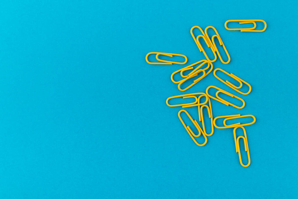 Colored paper clips. Yellow paper clips macro close up isolated on a blue background with copy space. - Photo, Image